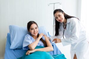 Asian young female doctor with syringe to the arm of Asian young female patient on Bed for better healing In the room hospital background.